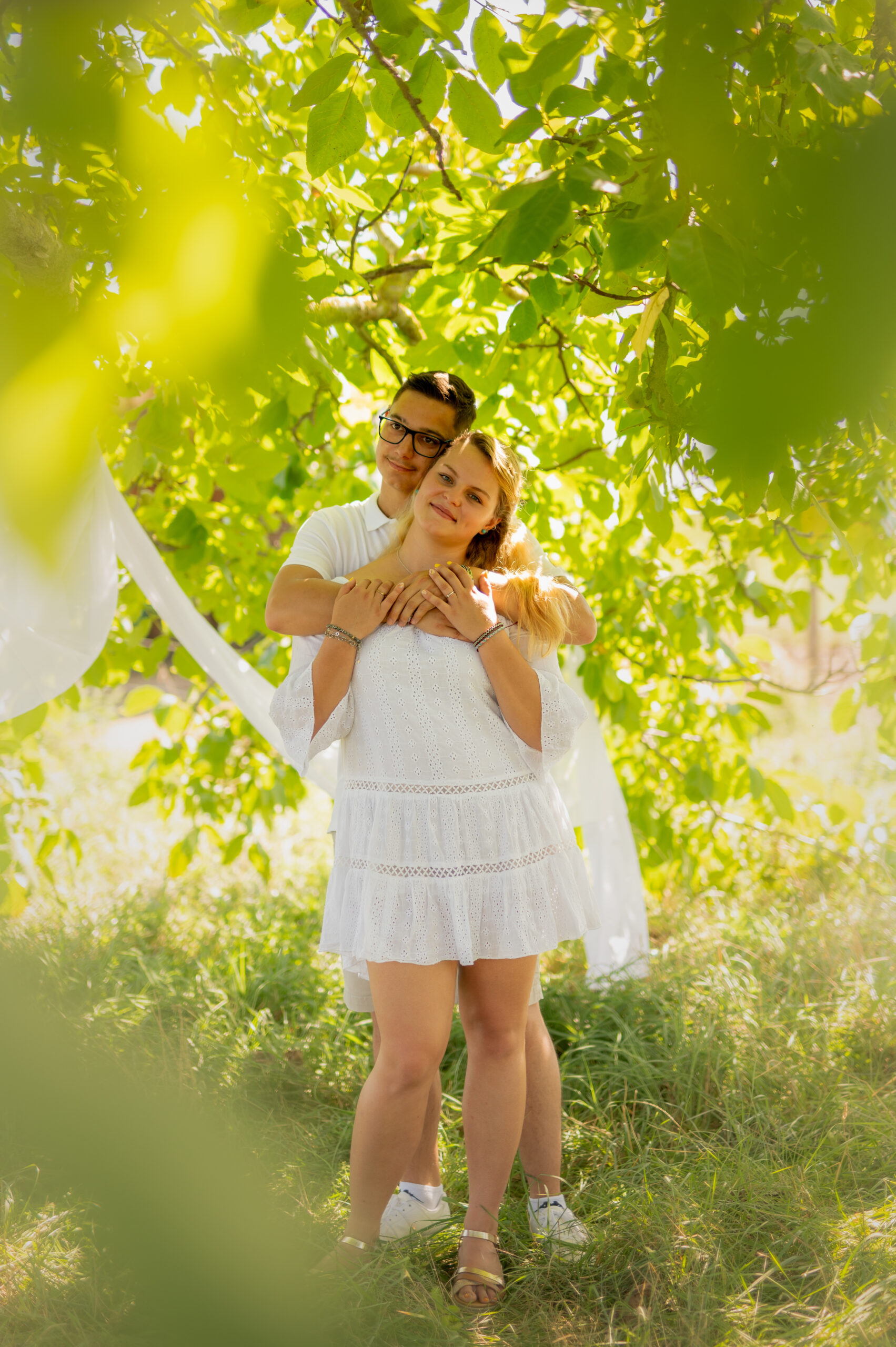 photographe professionnelle couple amour complicité tendresse extérieur arbre foret blanc voilage couleur naturelle regard amoureux habits blancs jeunes jeunesse